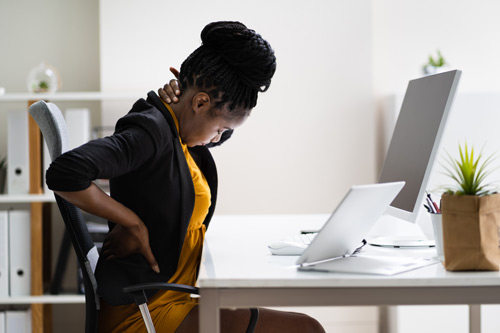 office worker sitting at her desk complaining of back and neck pain due to bad sitting posture