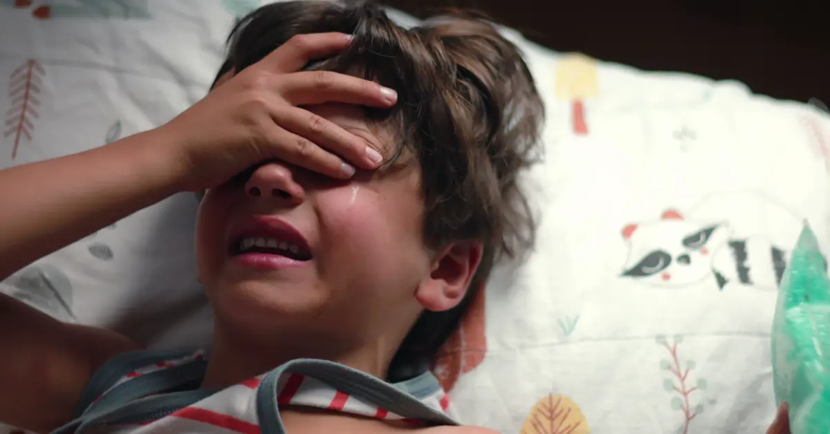 Young boy in bed at night, upset and covering his eyes with one hand