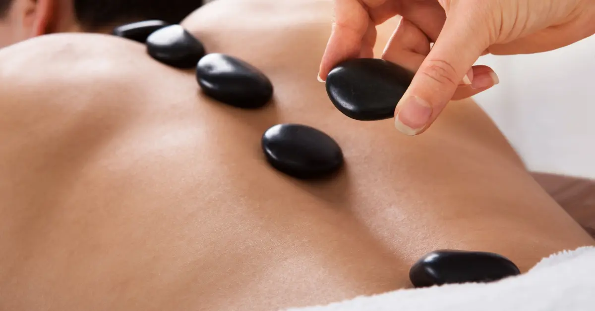 Therapist placing smooth black hot stones in a line along a client's back