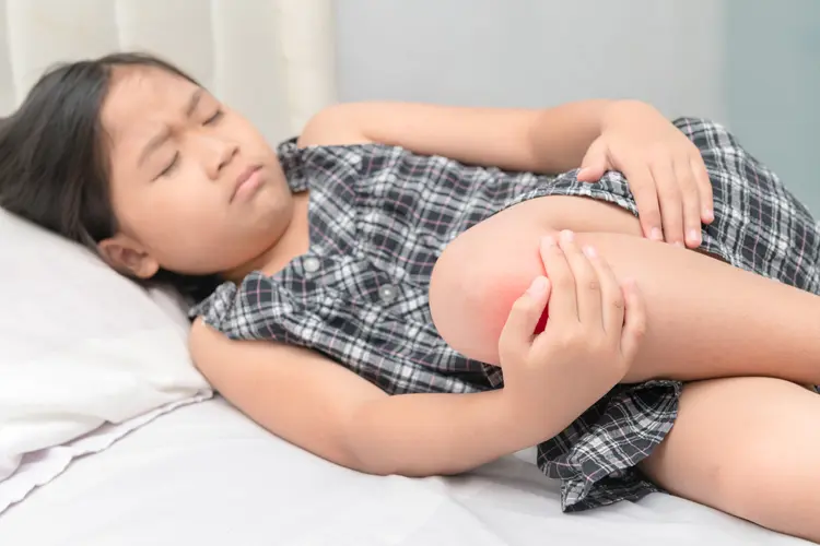 Young girl lying in bed, holding her sore knee