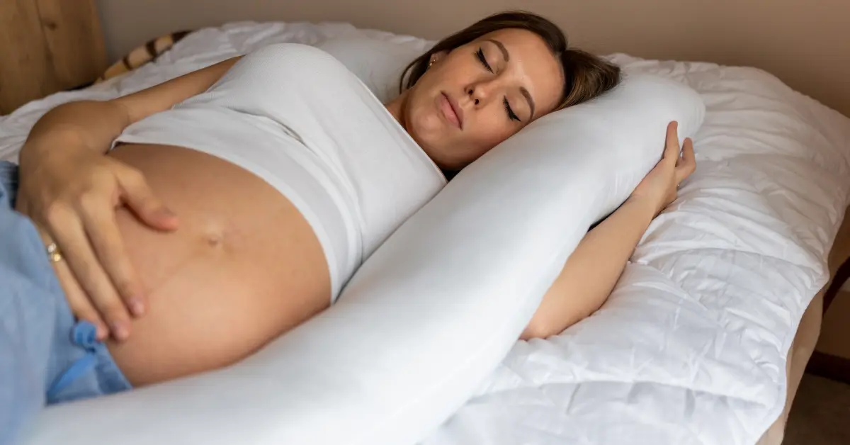 Pregnant woman lying awake on her side in bed at night, one hand resting on her belly.