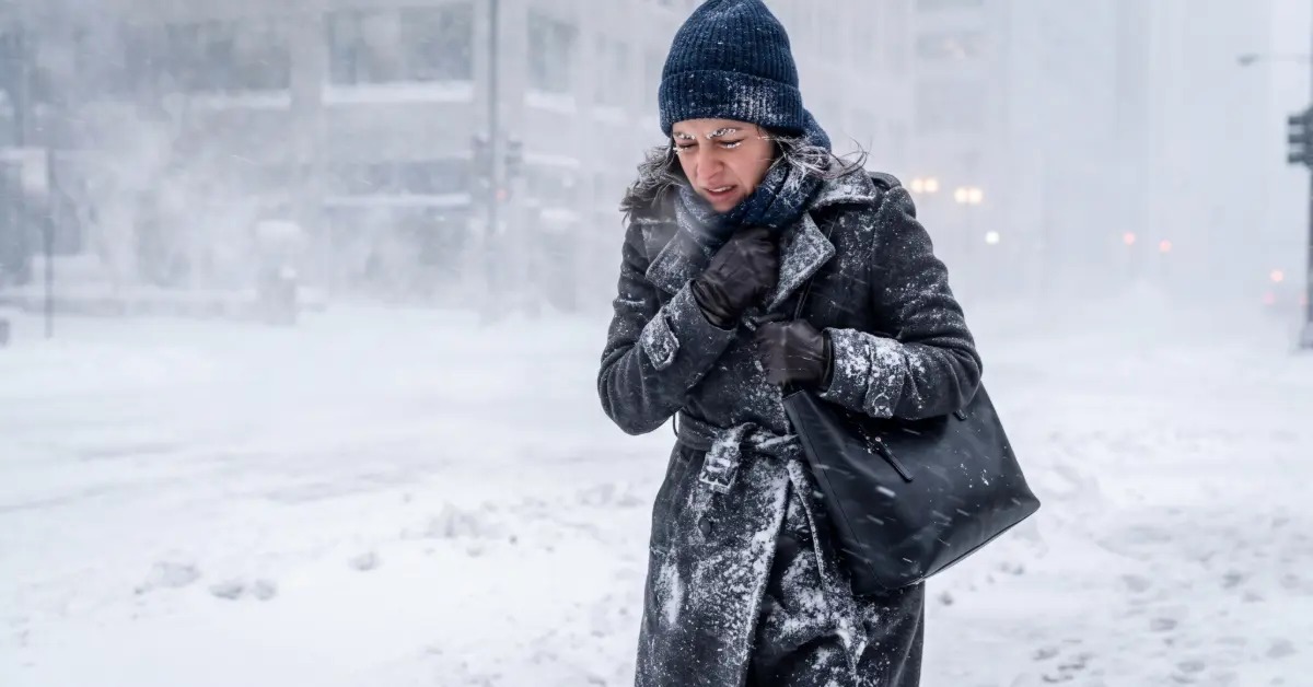 Woman hunched against blowing snow on a winter street, holding her coat closed